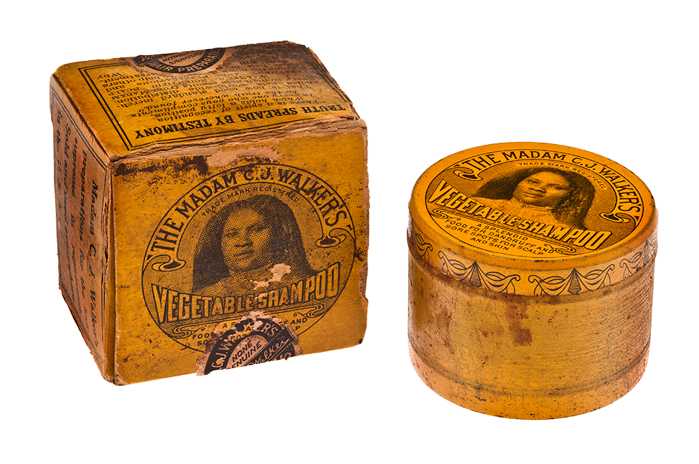 A shampoo tin and its box. On the lid of both the box and the tin lid is an image of Madam C.J. Walker with text that reads “The Madam C.J. Walker’s Vegetable Shampoo. Trade Mark Registered. A splendid food for dandruff and sore spots for scalp and skin.” On the side of the box appear to be testimonies about the product. The packaging is orange. 