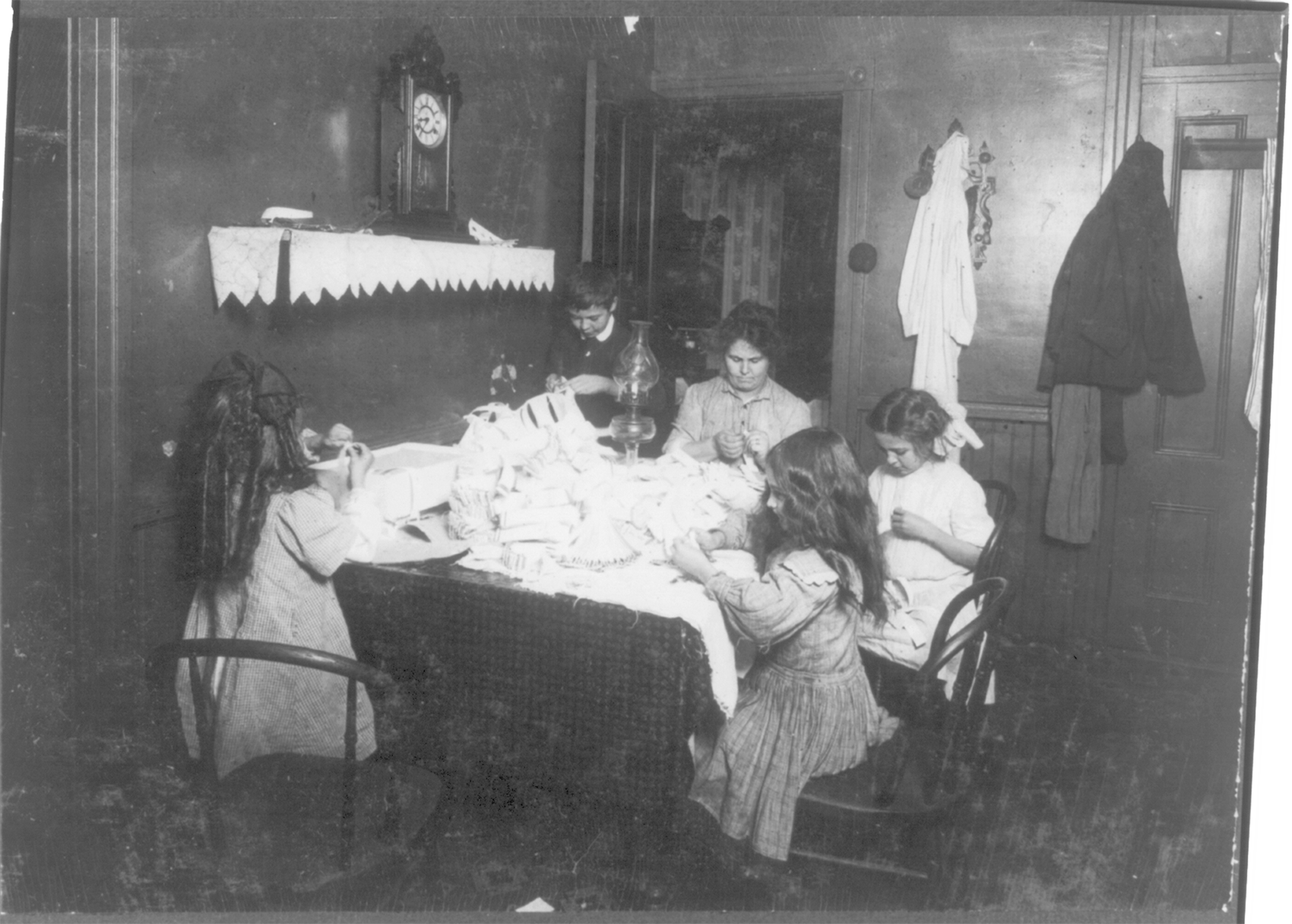 Photograph of a mother, her one son, and three daughters working around the table making hose supporters inside their house.