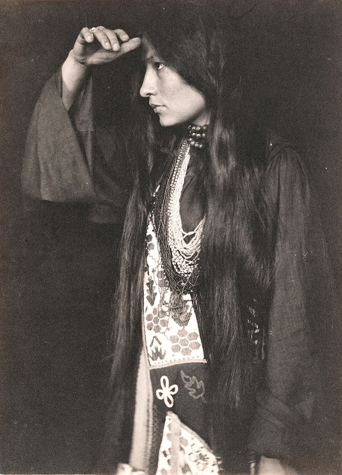 A photograph of Zitkala-Sa in profile. She is facing to her right with one hand on her brow, wearing clothing from her tribe. 