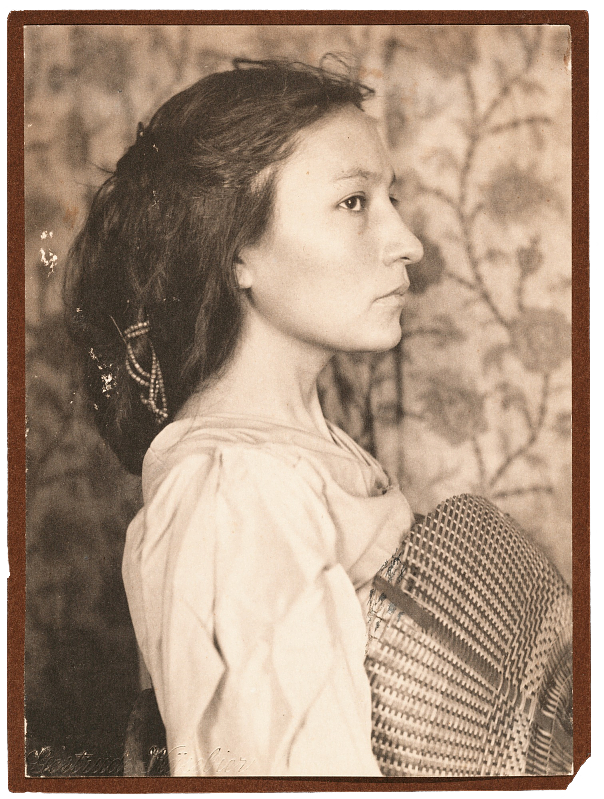 A photograph of Zitkala-Sa in profile facing to her left. She is holding a basket and wearing western clothing. 