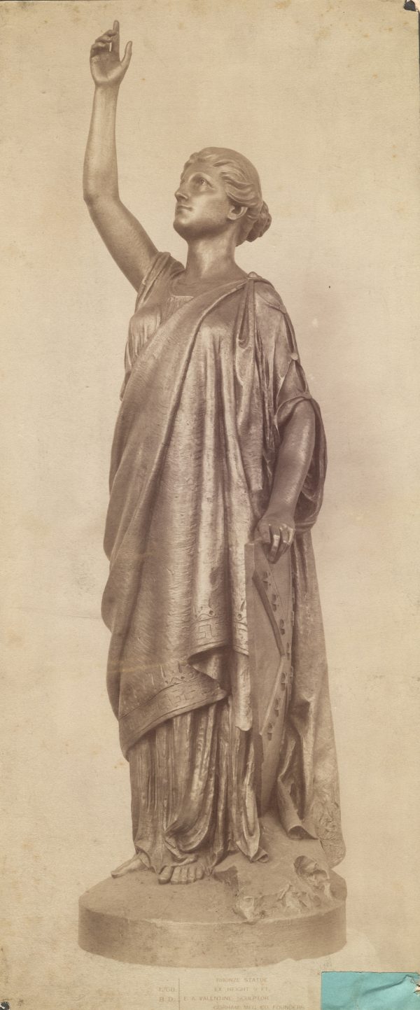 Photograph of a bronze statue called “Miss Confederacy.” Her hair is tied in a bun and she is dressed in a robe that is reminiscent of Greco-Roman fashion. Her right-hand is lifted towards the sky along with her face. This statue was created to sit atop the monument to Jefferson Davis in Richmond, Virginia. Davis was the president of the Confederate States of America.