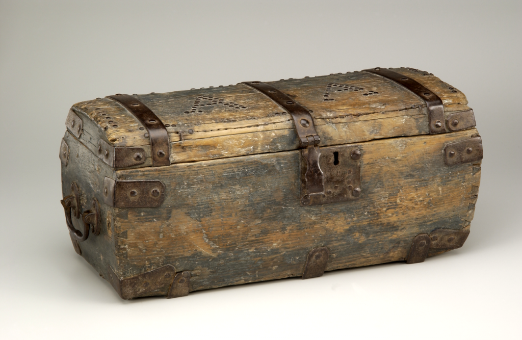 A 17th century rectangular wooden hope chest with metal carrying handles on each, an internal lock, metal bands, and decorative tacks on the lid outlining the initials “AA.” Dimensions: 9 ½” high x 22 ½” long x 10” wide.